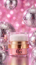  cosmetic jar with a white puff applicator, featuring a gold band and a pink shade visible through the clear container. The jar is set against a festive background of pink bokeh lights and silver disco ball ornaments.